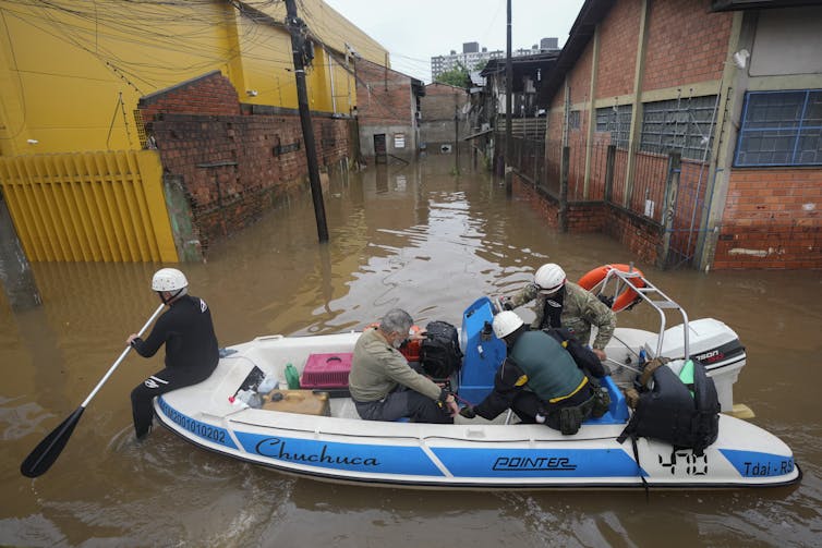 People sit in a boat among flooded buildings.
