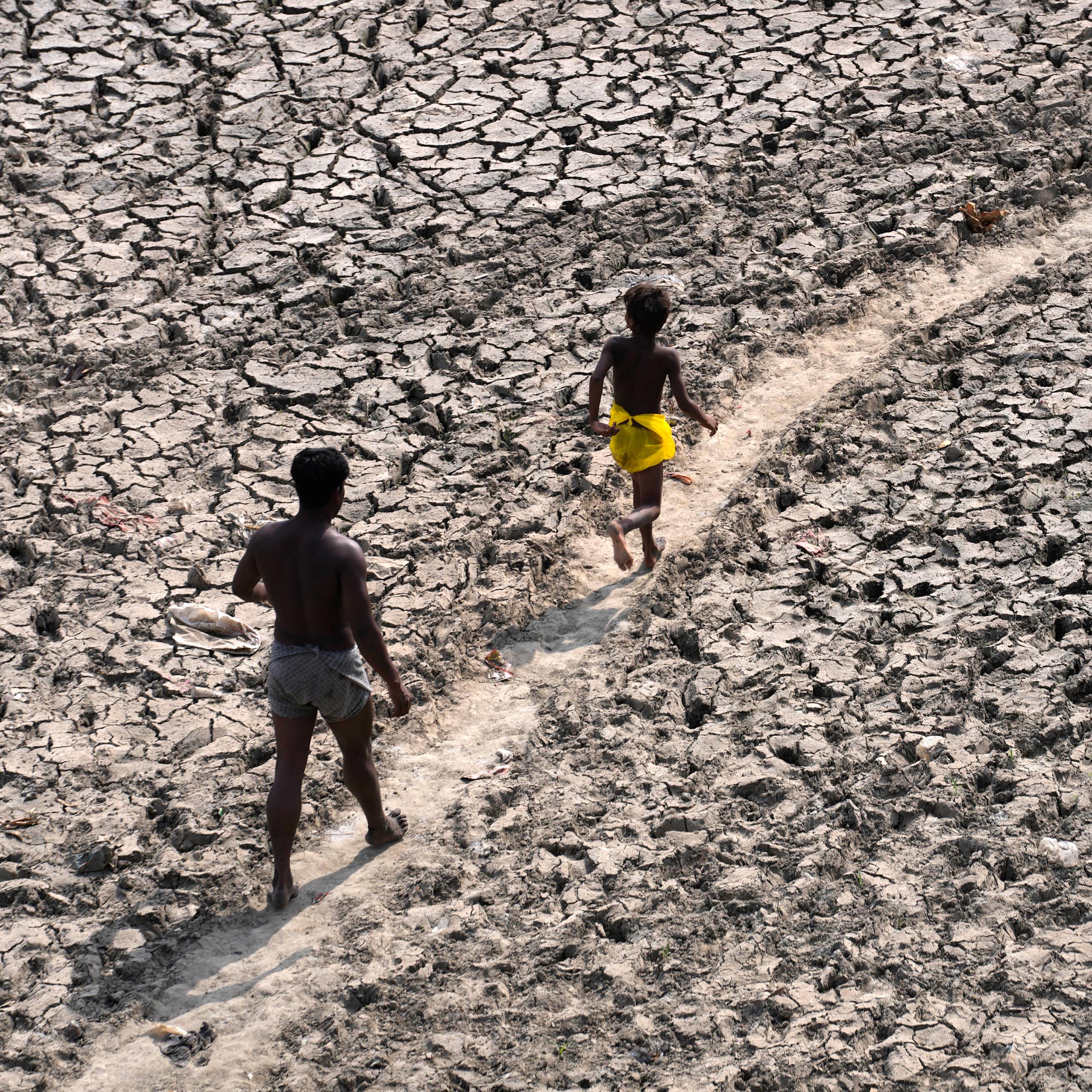 A man and a boy walk along a dried river bed.