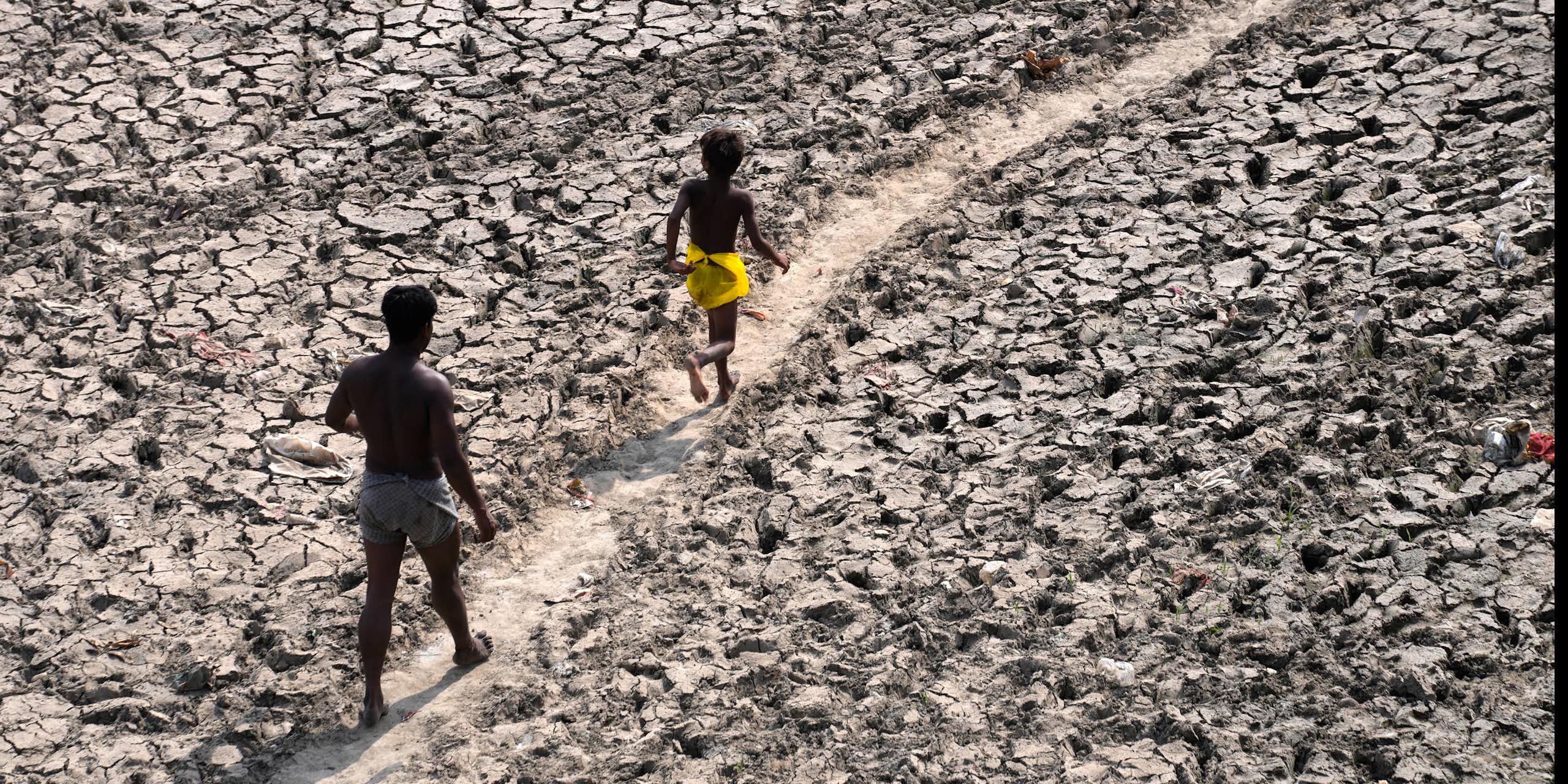 A man and a boy walk along a dried river bed.