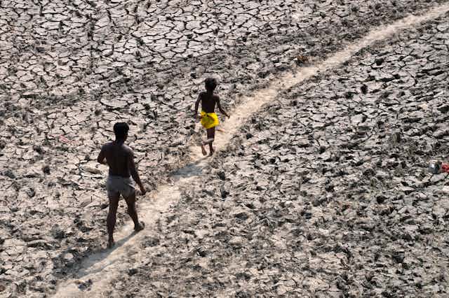 A man and a boy walk along a dried river bed.