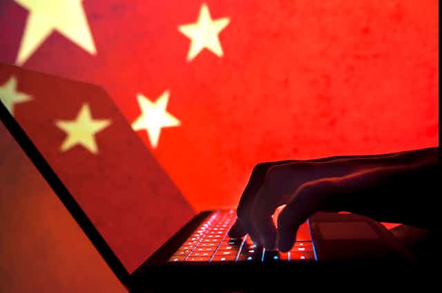 A silhouette of a hand on a laptop is seen in front of a Chinese flag.