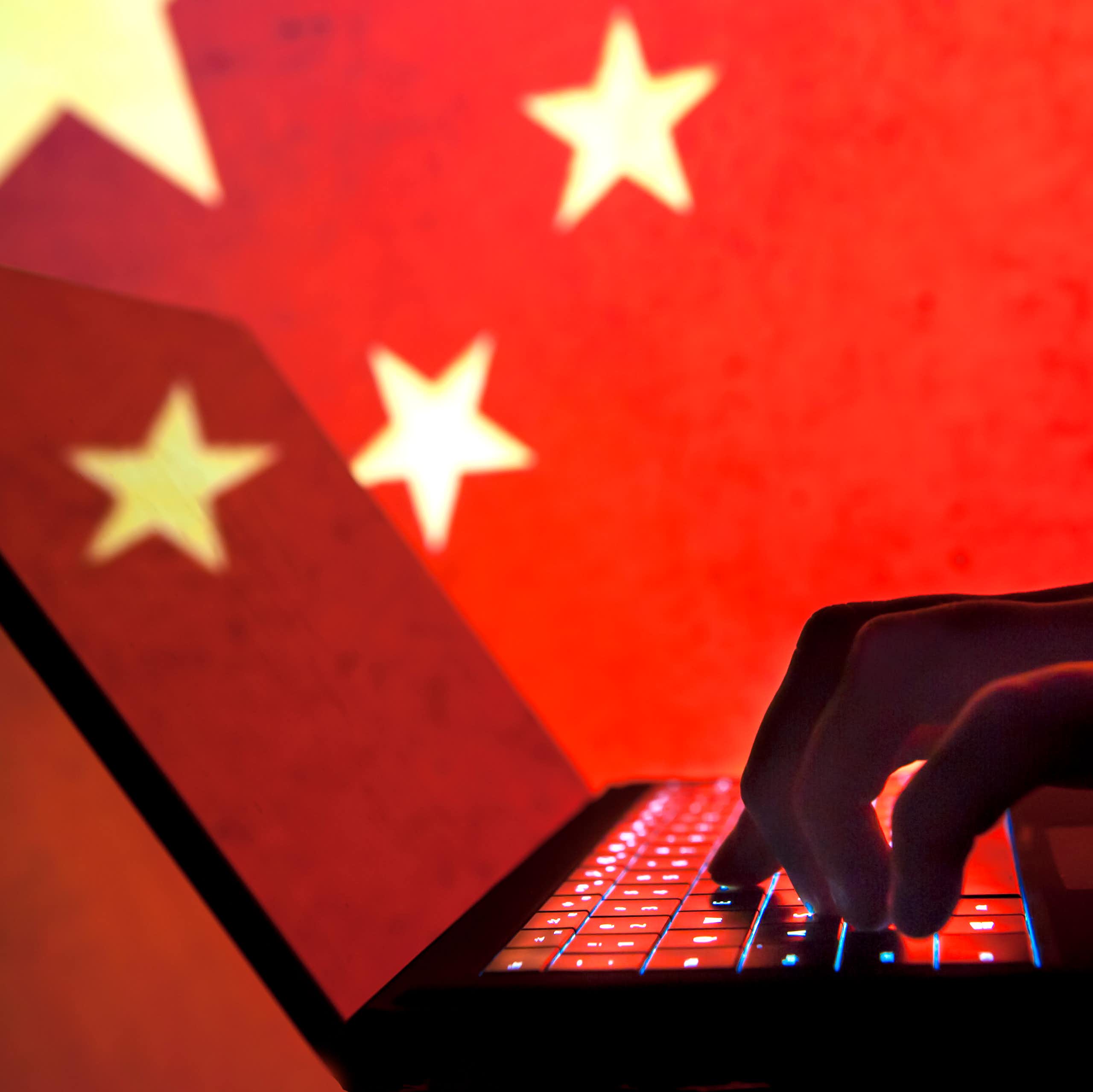 A silhouette of a hand on a laptop is seen in front of a Chinese flag.