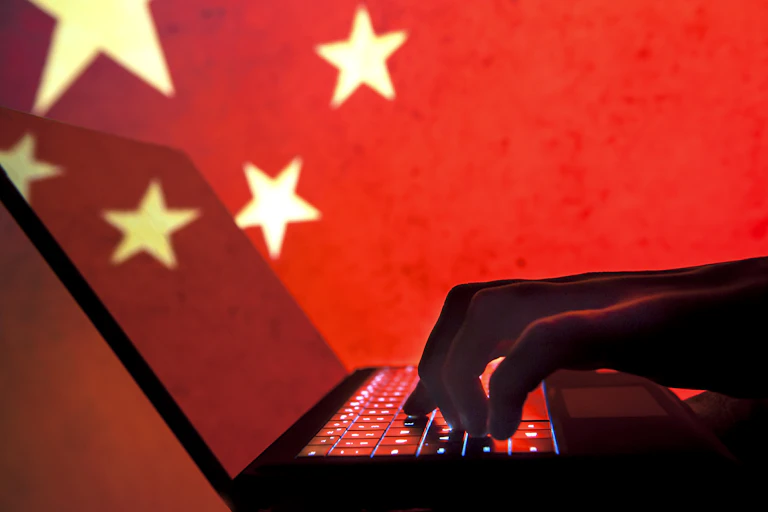 A silhouette of a hand on a laptop is seen in front of a Chinese flag.