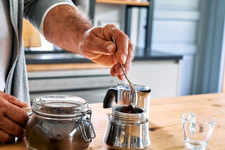 Man preparing Italian style coffee at home, adding coffee to pot
