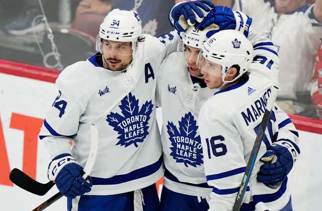 Three hockey players in maple leafs jerseys carrying hockey sticks.