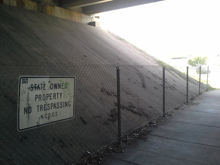 A white sign warning against trespassing is attached to a simple metal fence next to a concrete bank.
