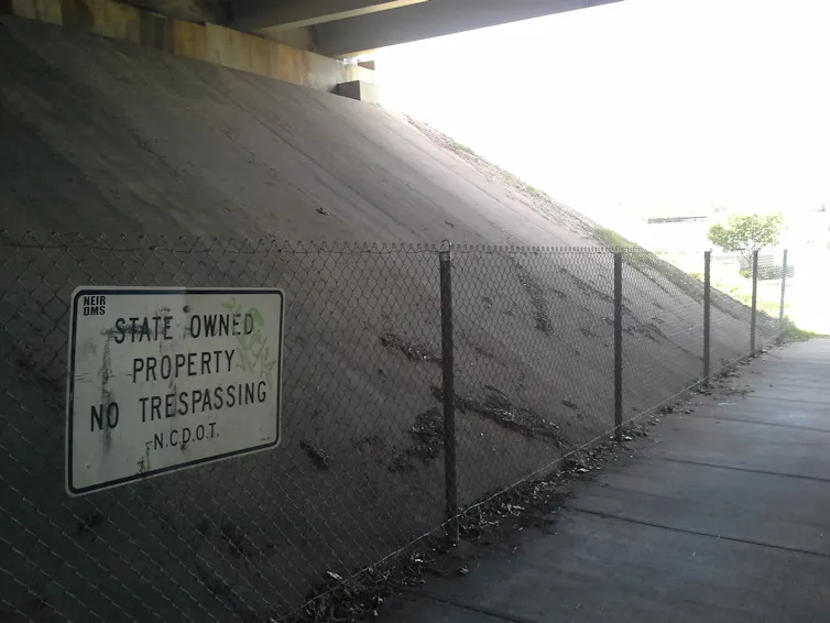 A white sign warning against trespassing is attached to a simple metal fence next to a concrete bank.