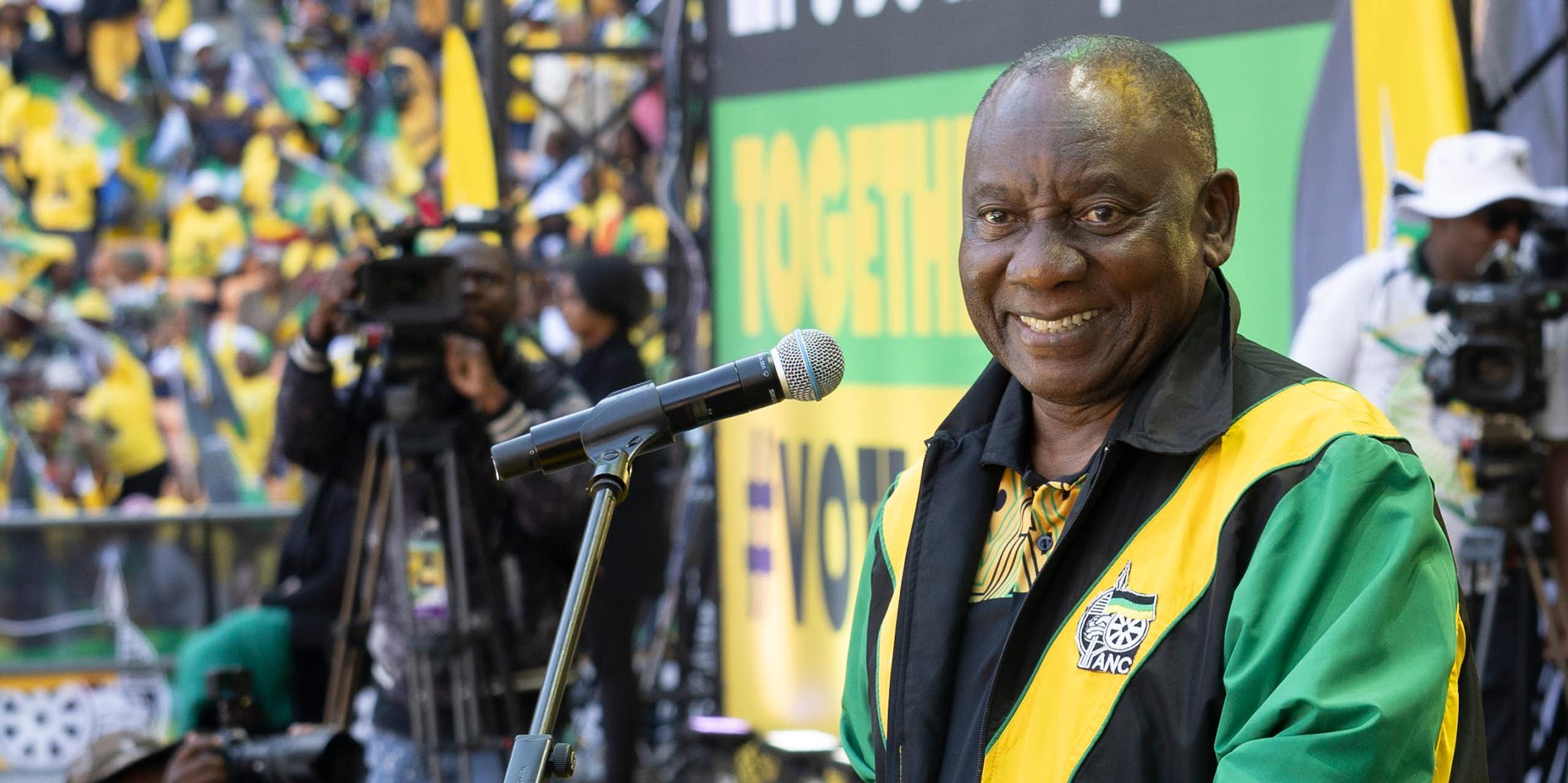 A man dressed in a green, yellow and black jacket standing in front of a microphone smiling at the camera.