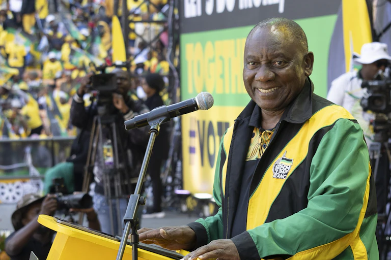 A man dressed in a green, yellow and black jacket standing in front of a microphone smiling at the camera.