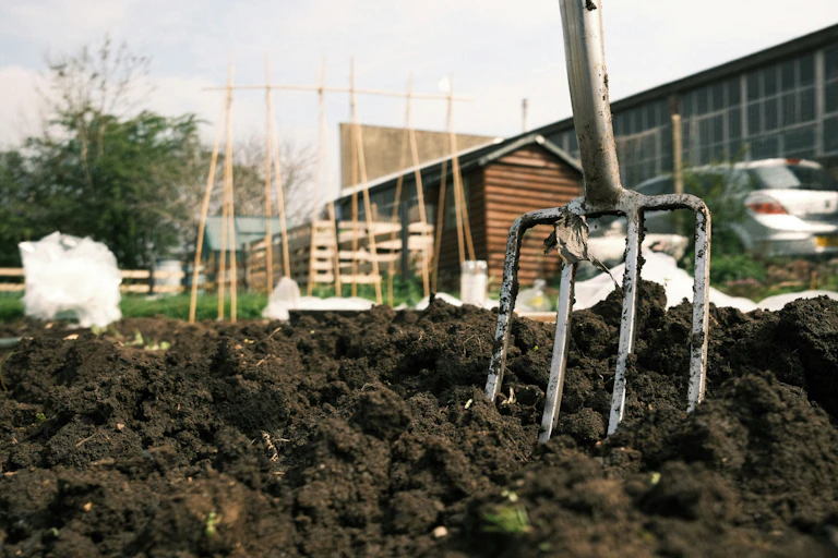 A garden fork in brown earth in an urban setting.