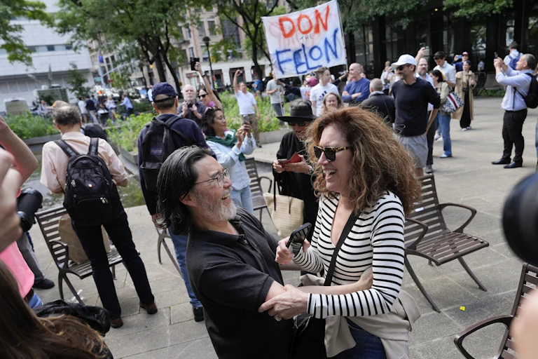 Smiling people embrace while in the background others hold signs and smile.