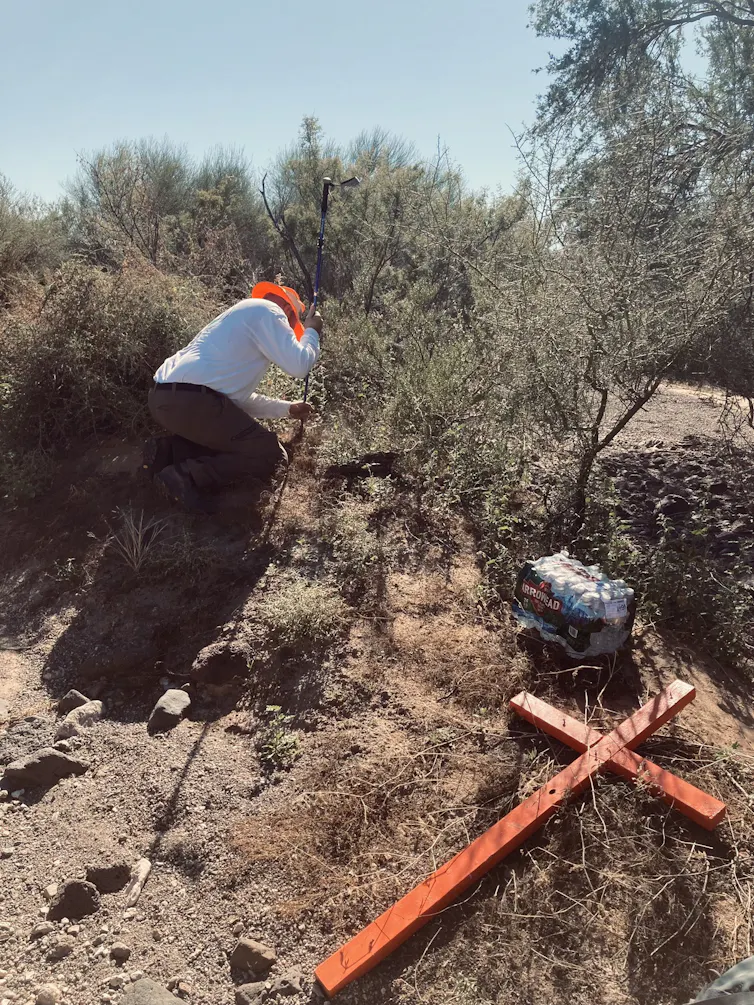 a man digs into the dirt, an orange cross on the ground by his side