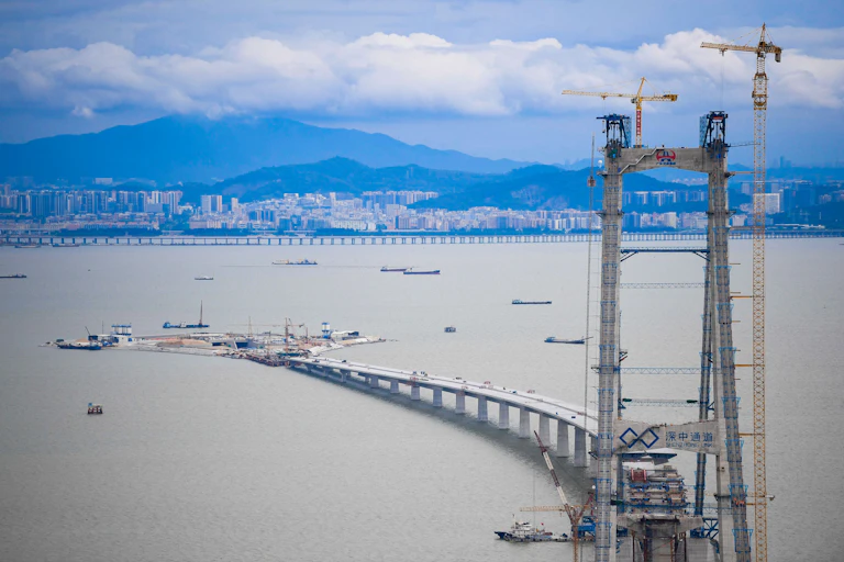 scaffolding and boats around a partially constructed bridge with shoreline in background