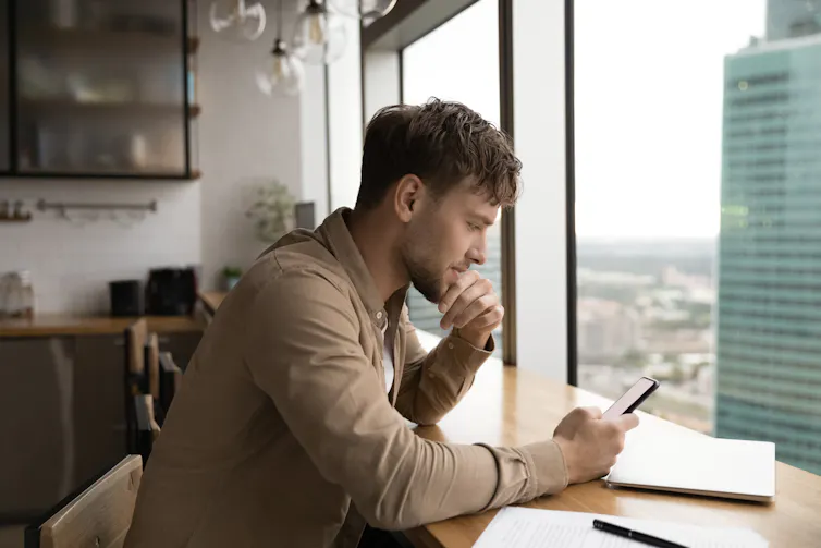 A young man seated at a window looking at his phone