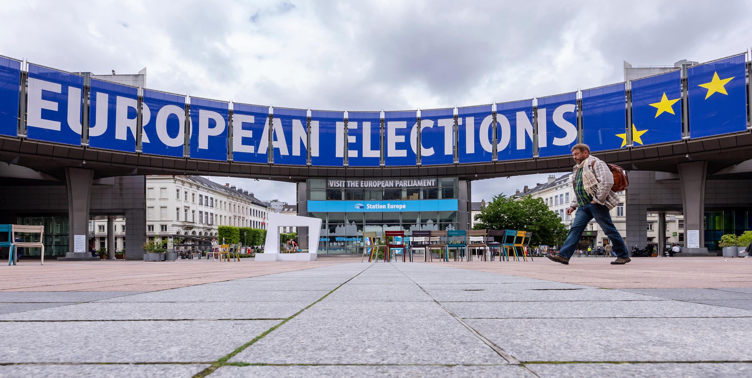 A man walks past a blue and white sign that reads European Elections