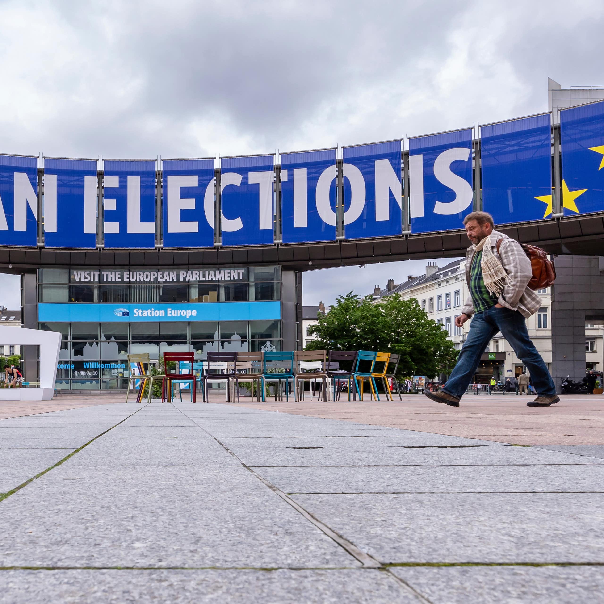 A man walks past a blue and white sign that reads European Elections