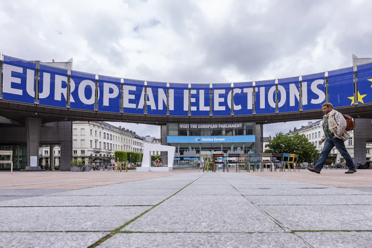 A man walks past a blue and white sign that reads European Elections