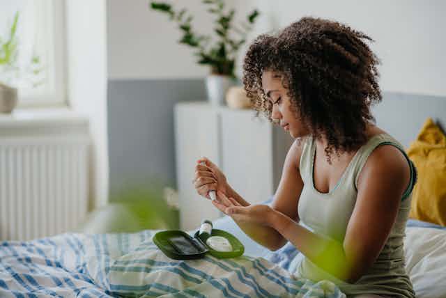 A young woman in her bedroom holds a glucometer with test strip.