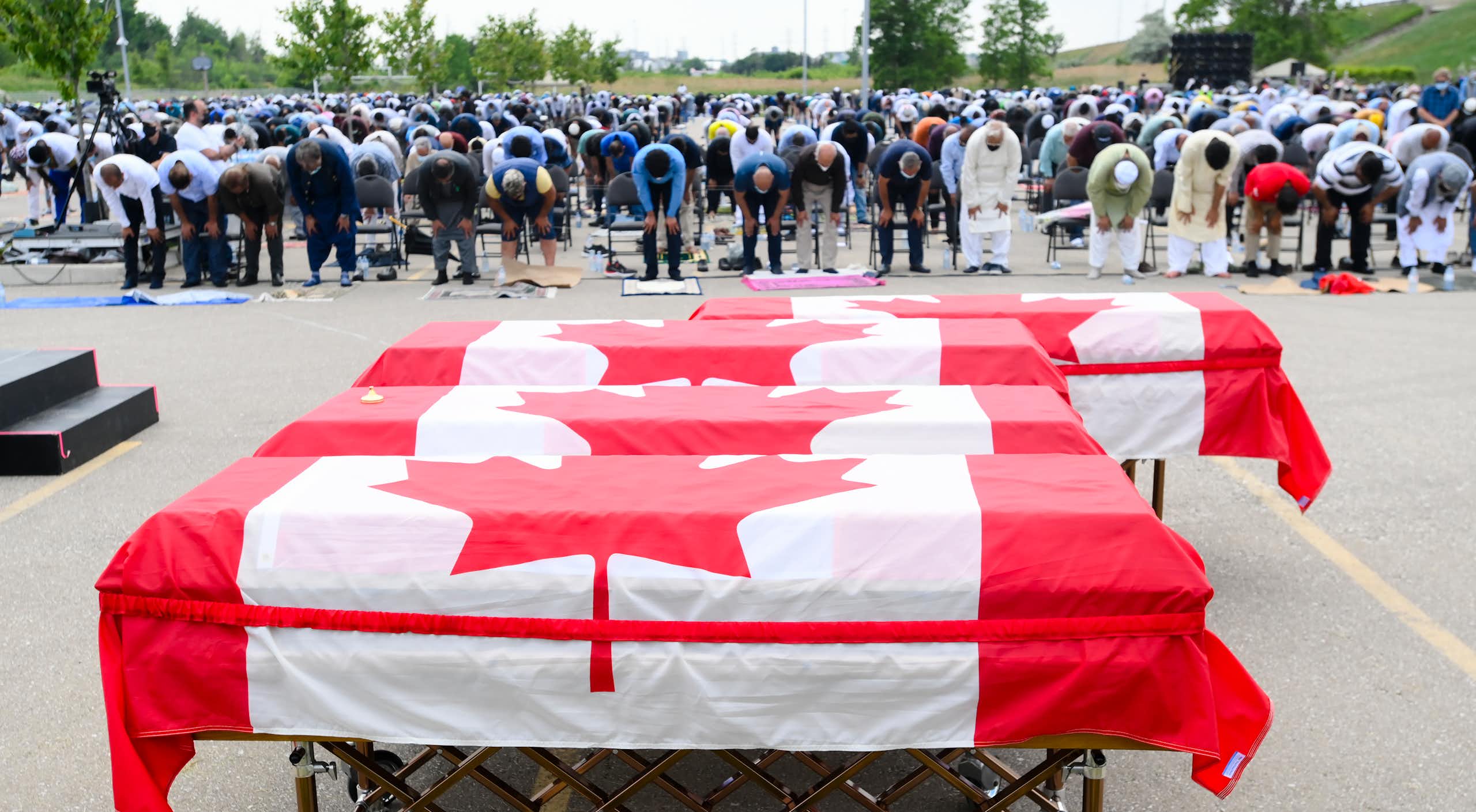 People pray in front of a row of coffins covered in Canadian flags.
