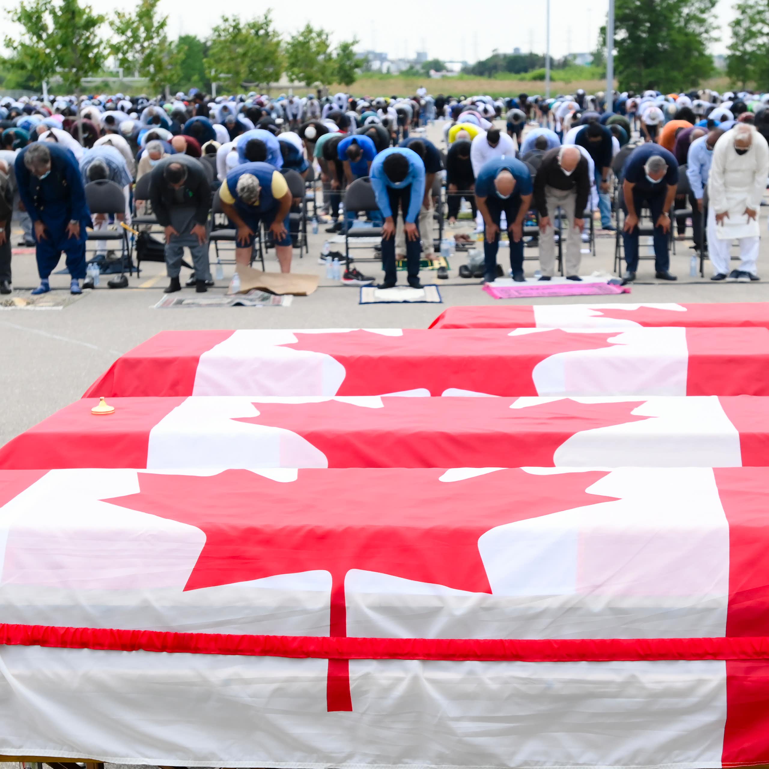 People pray in front of a row of coffins covered in Canadian flags.