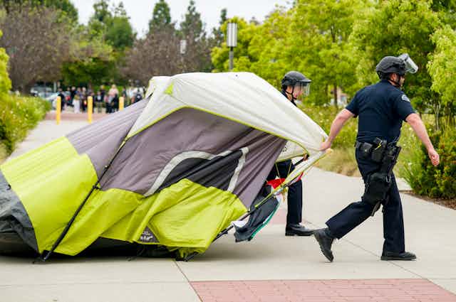 Two police officers drag a tent.