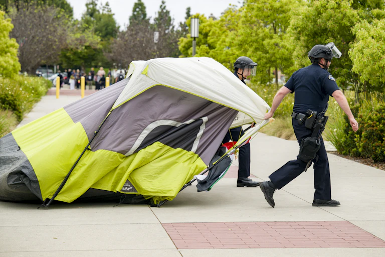 Two police officers drag a tent.