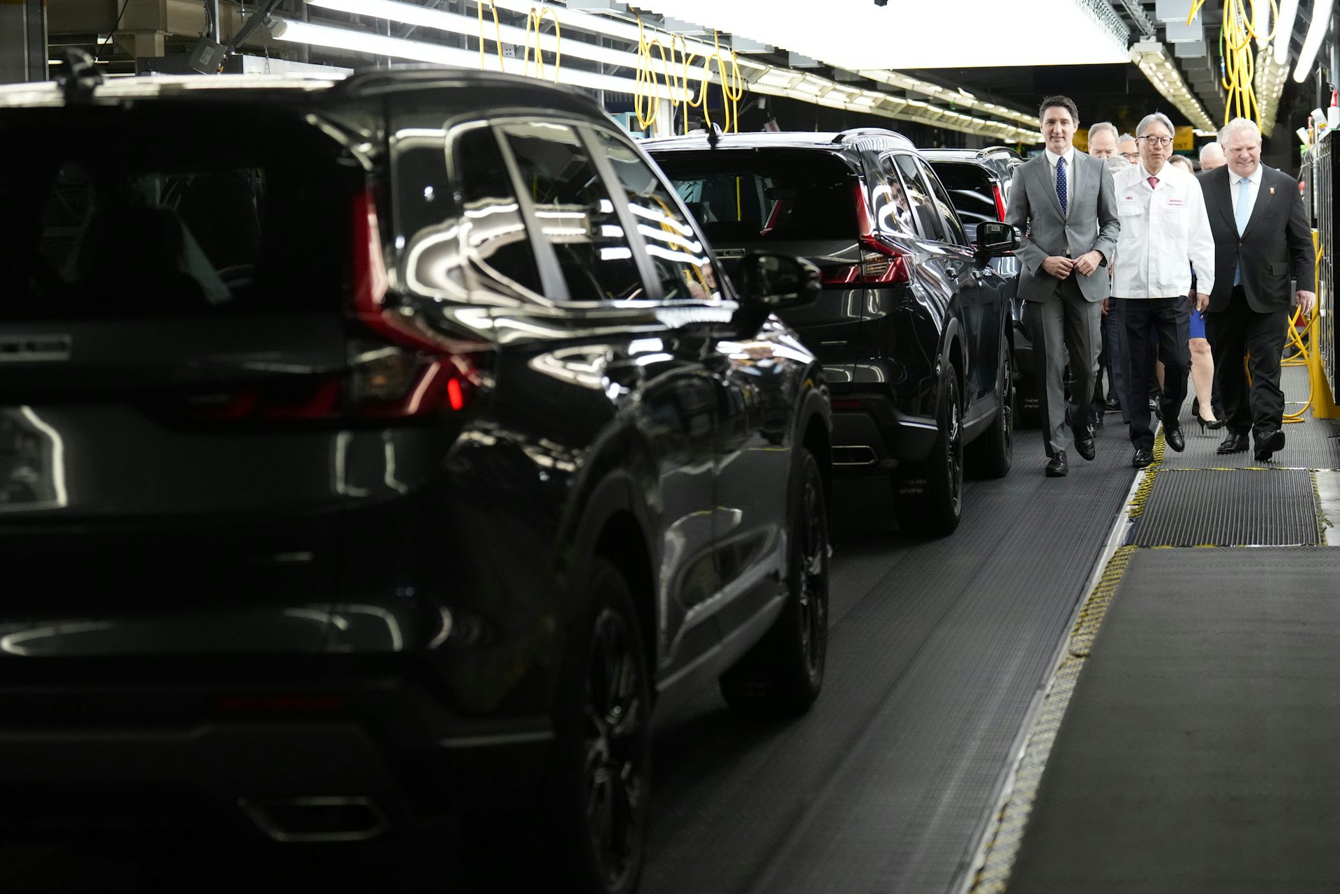 Three men walk beside an EV assembly line.