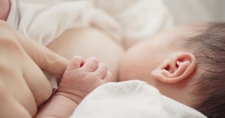 baby breastfeeding and holding mother's finger