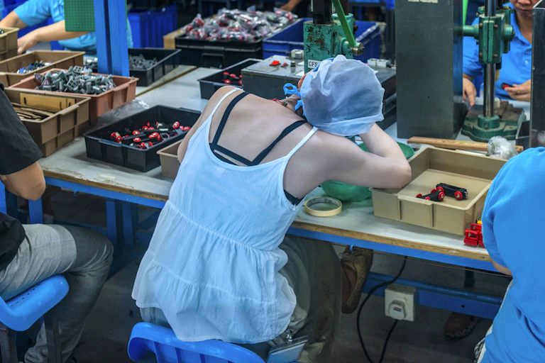 A woman slumps at her worktable in a factory.