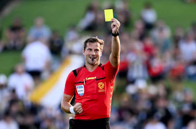 An A-League soccer referee holds aloft a yellow card