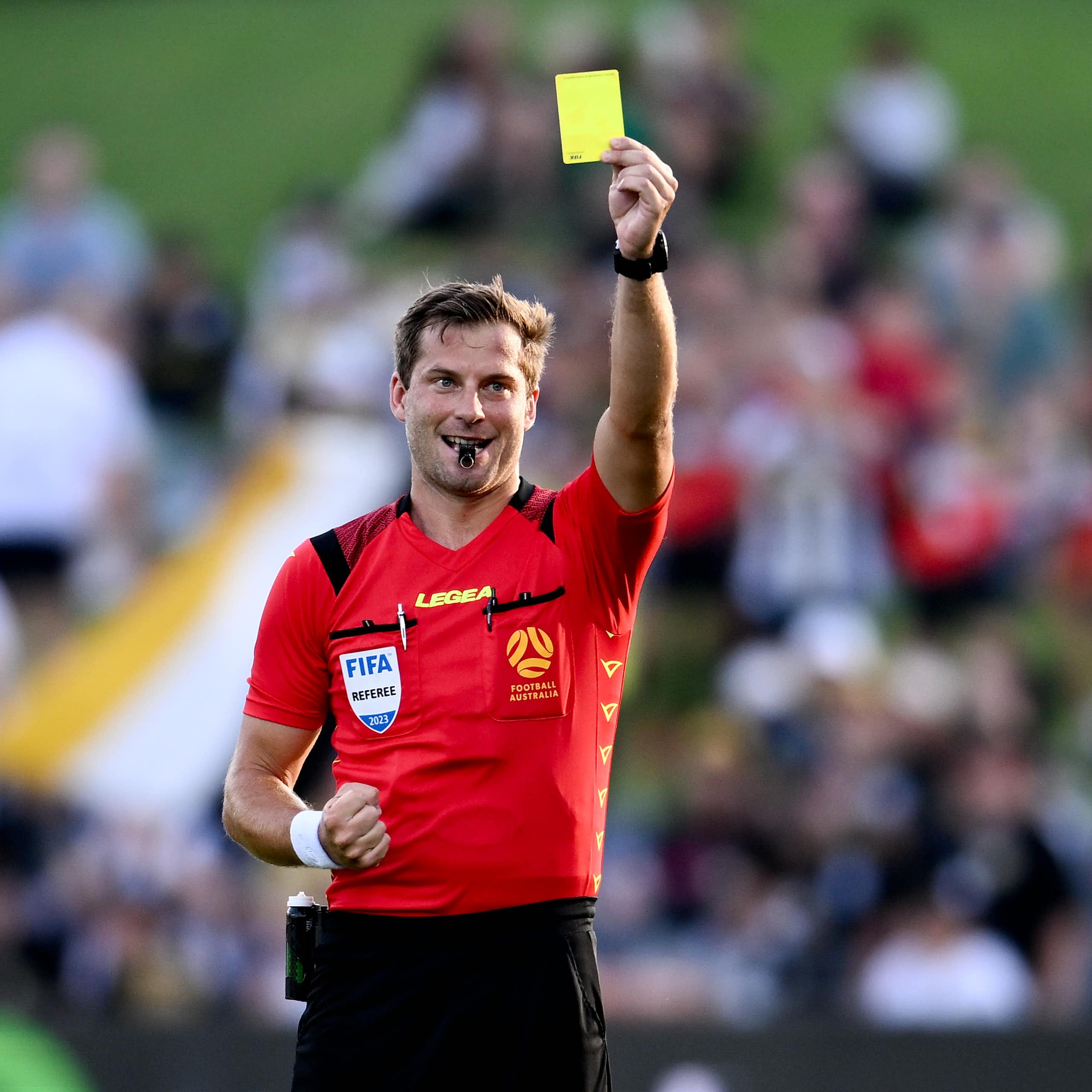 An A-League soccer referee holds aloft a yellow card