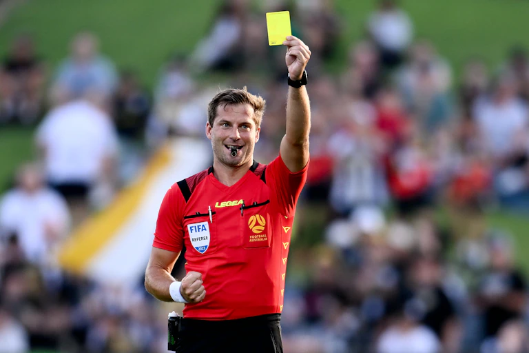 An A-League soccer referee holds aloft a yellow card