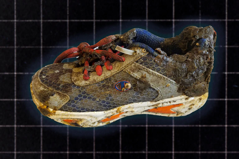 A running shoe covered in grime and barnacles displayed on a dark grid background.
