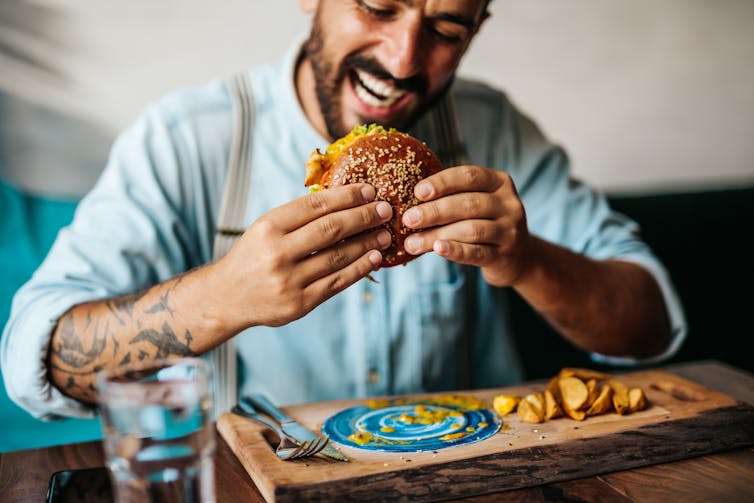 Homem sentado no restaurante e saboreando um hambúrguer.