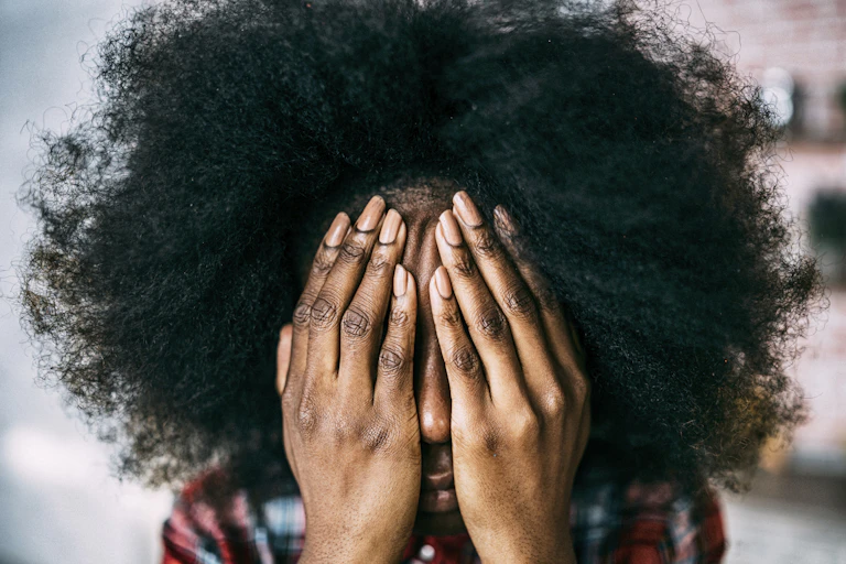 Head and shoulders view of a person with hands over their face