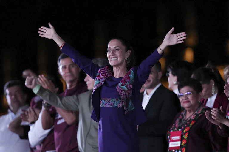 A woman in a purple dress holds her hands aloft in celebration.