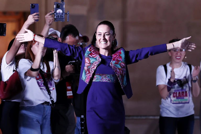 Claudia Sheinbaum holds out her arms in triumph following her election victory.