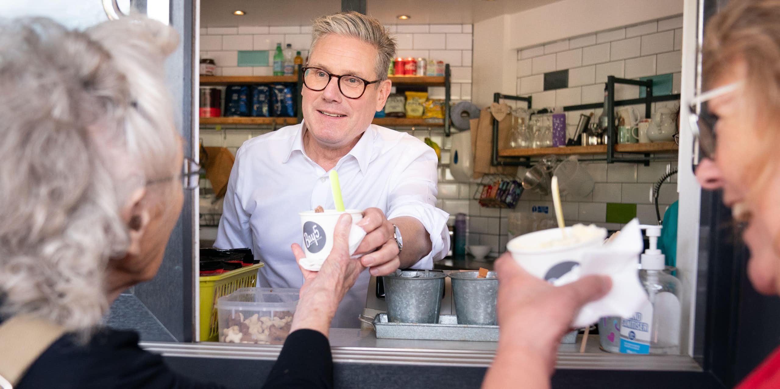 Keir Starmer handing a customer an ice cream from a hatch in the front of a shop. 