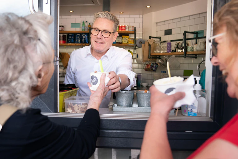 Keir Starmer handing a customer an ice cream from a hatch in the front of a shop.