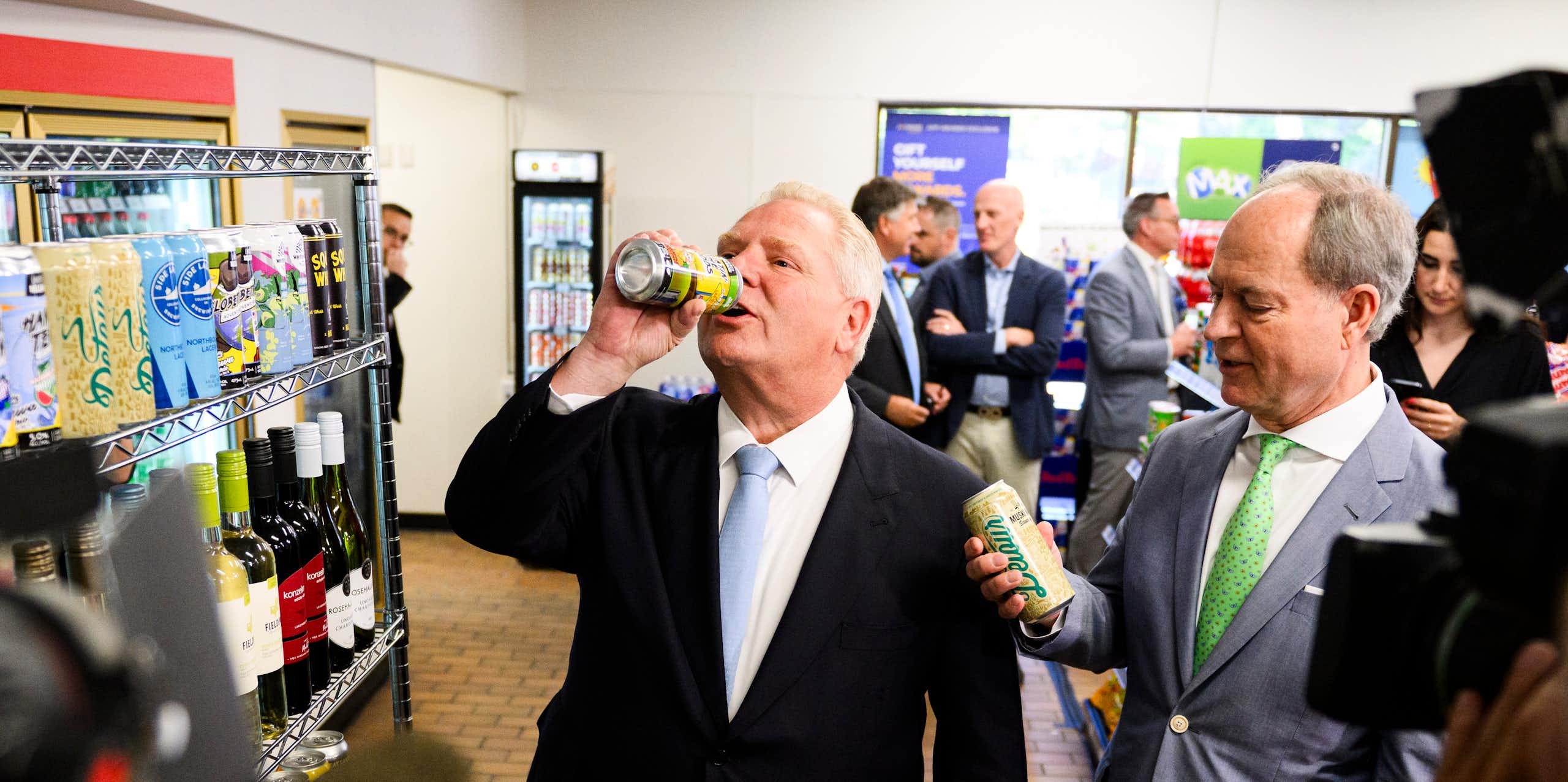 A balding man in a dark suit and pale blue tie appears to be slugging back a beer.