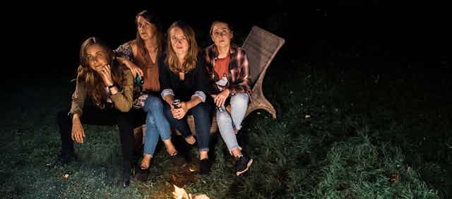 Four women seen sitting in the dark near a campfire.