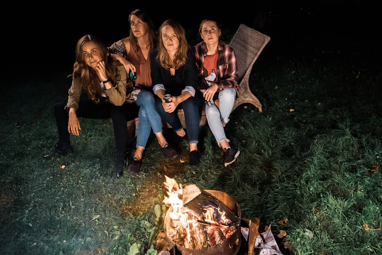 Four women seen sitting in the dark near a campfire.