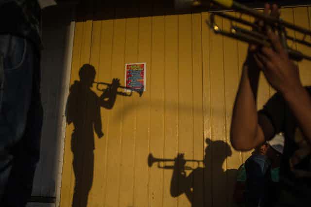 The silhouettes of men playing trumpets are seen on a wooden brown fence.