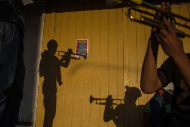 The silhouettes of men playing trumpets are seen on a wooden brown fence.