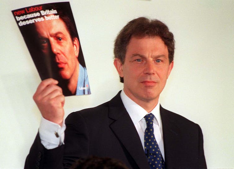 Tony Blair segurando o manifesto de seu partido de 1997, que tem seu rosto na capa.