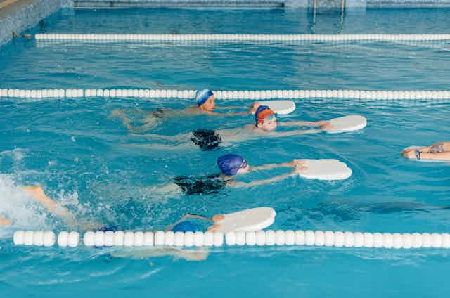 Des enfants nageant avec des planches dans une piscine