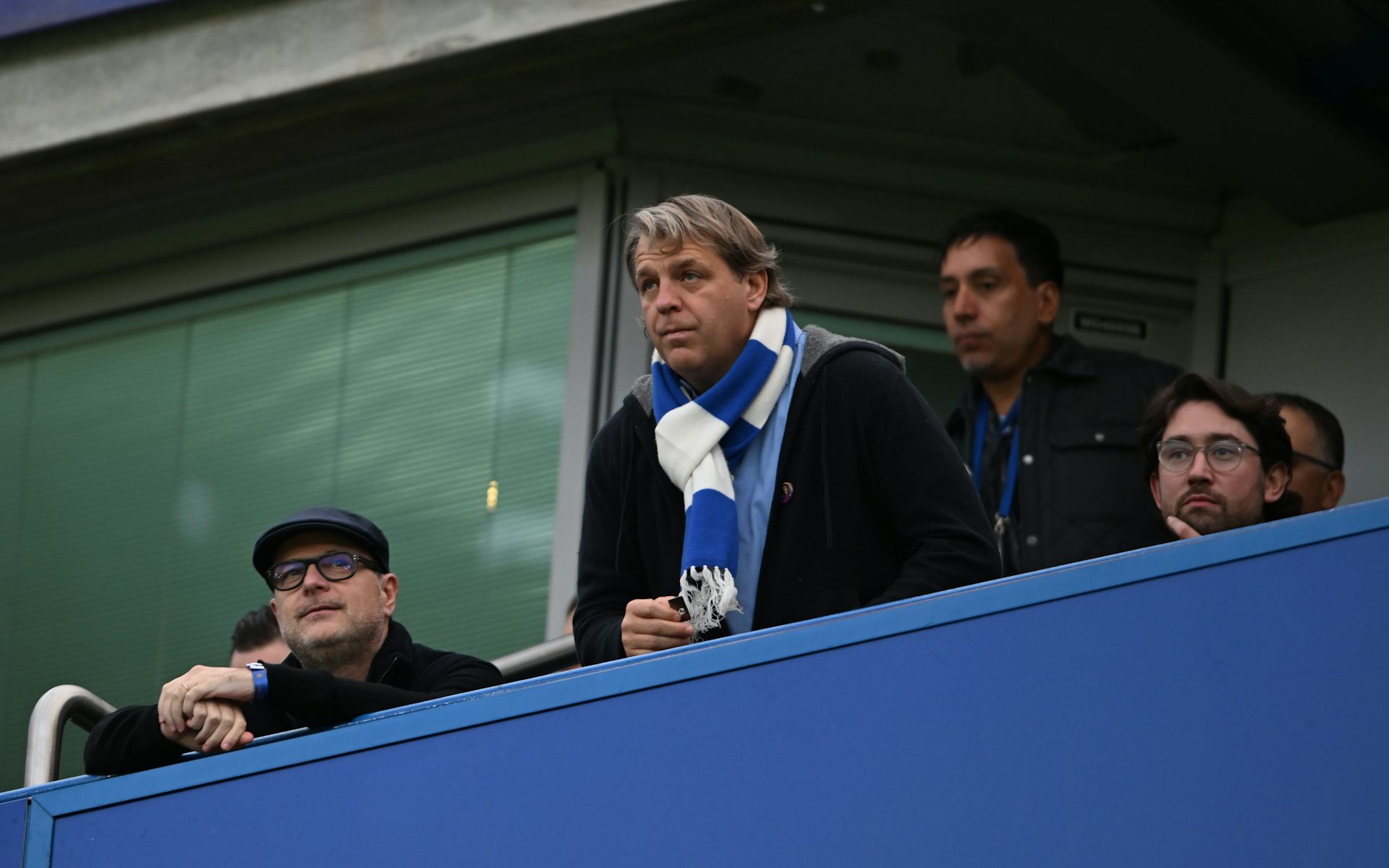 Todd Boehly wearing a blue-and-white scarf watching a game of football from the stands.