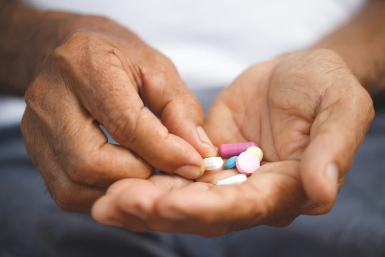 Un gros plan sur les mains d'un homme qui tient des comprimés de médicaments