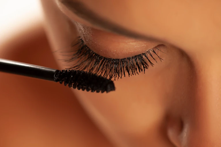 close up de uma mulher aplicando maquiagem de rímel nos cílios