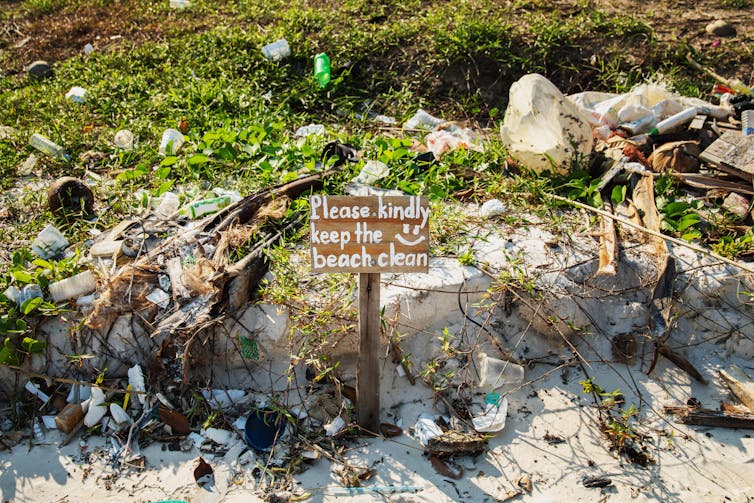 sign on trashed shoreline reads 'please kindly keep the beach clean :)'